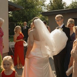 fredieme.photo - Alfred Wiśniewski - Panna młoda w sukni ślubnej z welonem, otoczona gośćmi weselnymi w ogrodzie, uchwycona z perspektywy pleców, z widocznym tatuażem motyla.