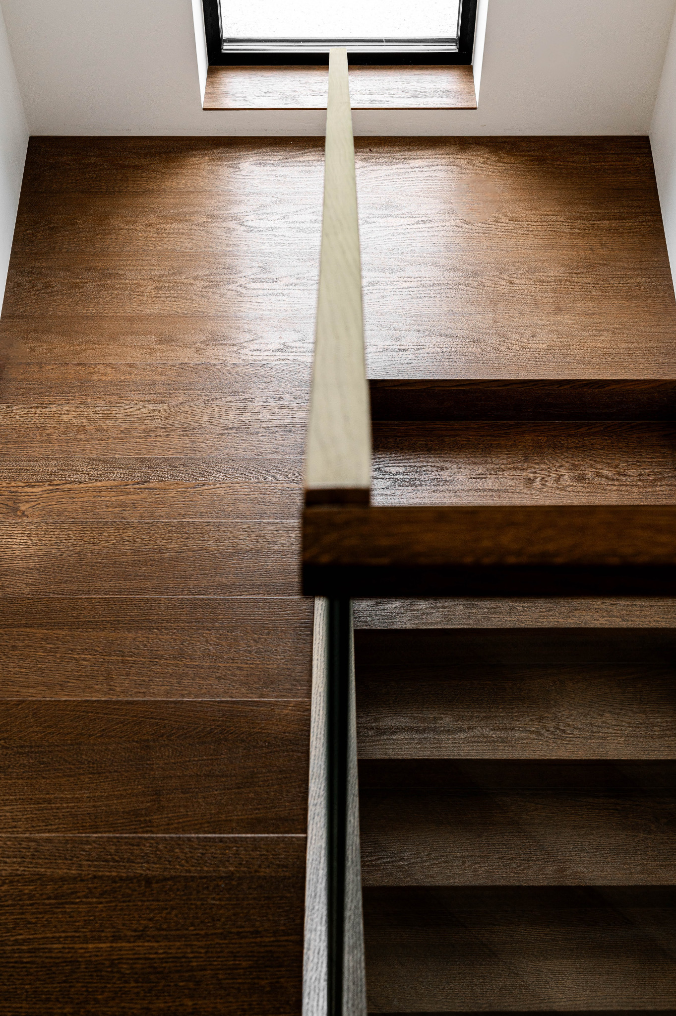 Drewniane schody z oświetleniem górnym, minimalistyczna balustrada. Nowoczesne wykończenie wnętrza z dbałością o detale i naturalne światło.