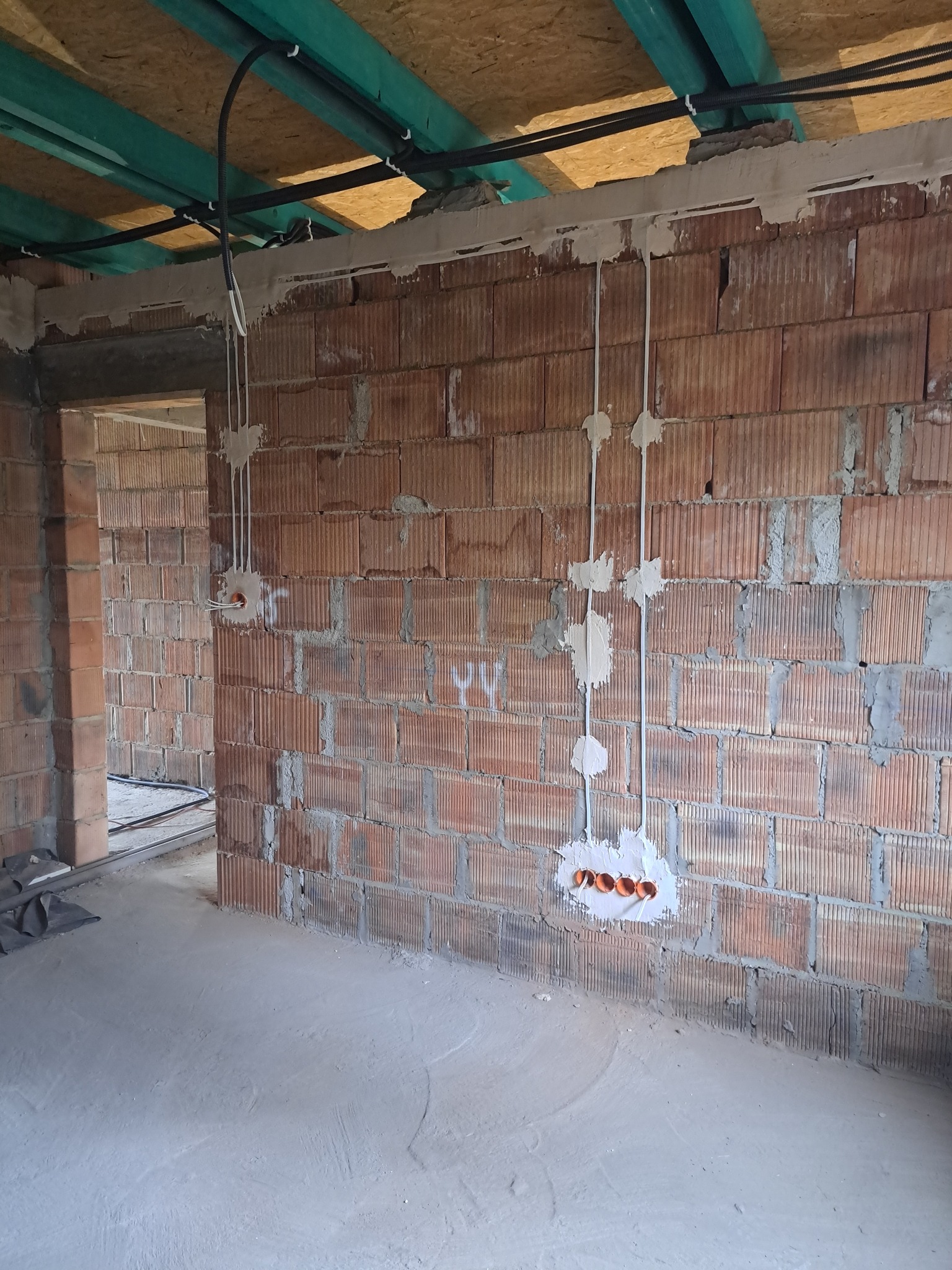 Instalacja elektryczna w surowym wnętrzu budynku w Mokrzyskach. Widoczne przewody i puszki elektryczne na ceglanej ścianie. Prace instalacyjne w trakcie realizacji.
