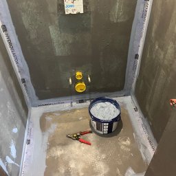 Mirosław Grzybek Wykończenia z Pasją - Hydroizolacja w kabinie prysznicowej w trakcie prac. Widoczna puszka JOMO, wiadro z masą uszczelniającą i narzędzia. Hydroelaston na taśmach uszczelniających.