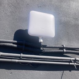 LinkSecure - Biała antena Nokia zamontowana na szarej ścianie zewnętrznej budynku, z widocznymi czarnymi kablami w peszlach i rurkach instalacyjnych.