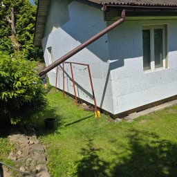 Przem-bud - Ocieplony budynek z widocznym styropianem, rynną i oknem. Na trawie stoi suszarka na pranie. Prace przygotowawcze do elewacji w słoneczny dzień.