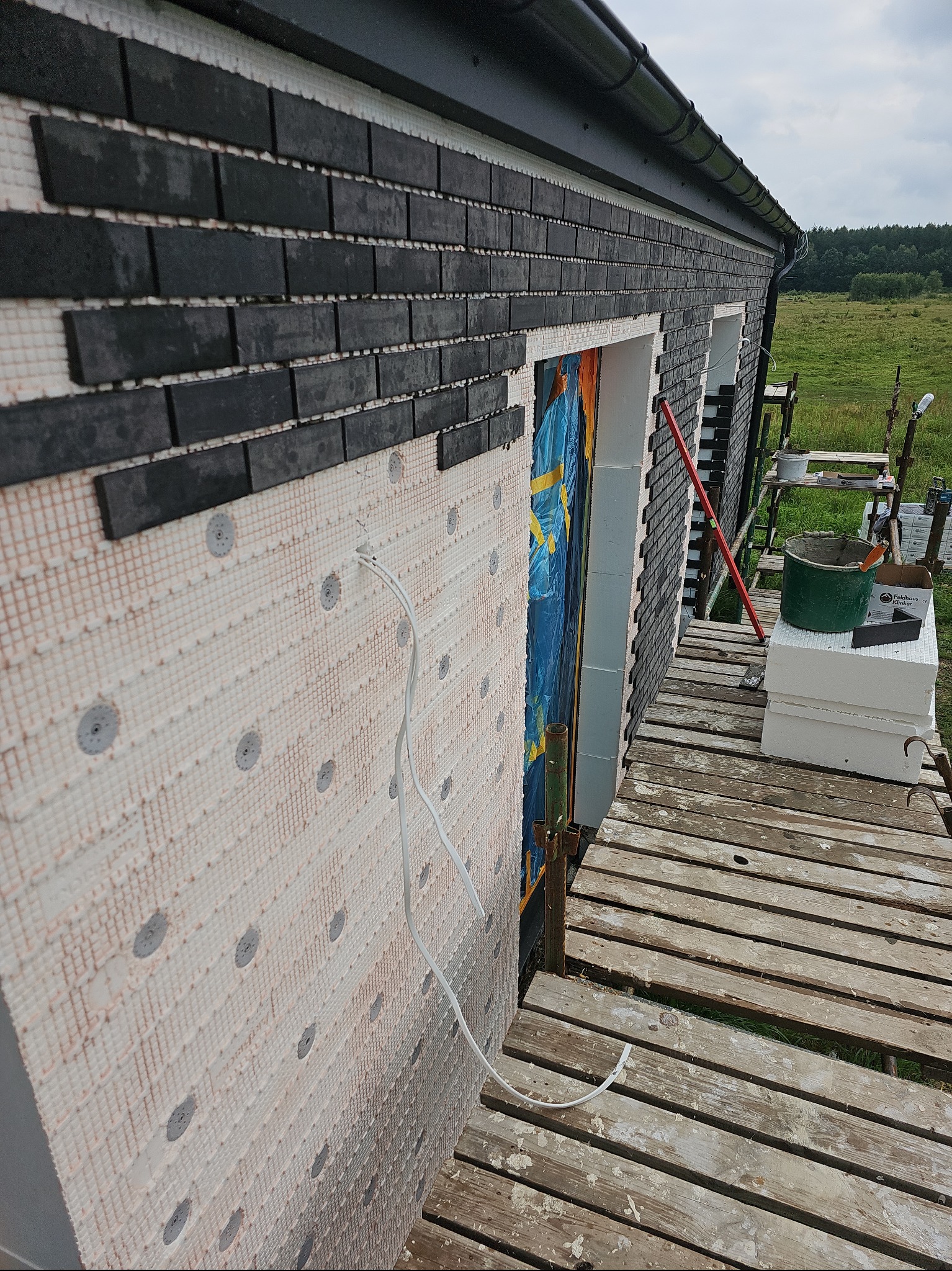 Wykonanie elewacji z klinkieru na ociepleniu budynku w Redzie. Widoczne rusztowanie i etap prac z częściowo ułożonymi płytkami klinkierowymi.