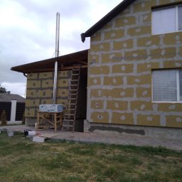VERTIKAL PLUS OLEH KOLOBOV - Ocieplanie budynku wełną mineralną, widoczne płyty izolacyjne i rusztowanie. Kominek z blachy wystaje ponad dach. Prace w toku, widok z zewnątrz.