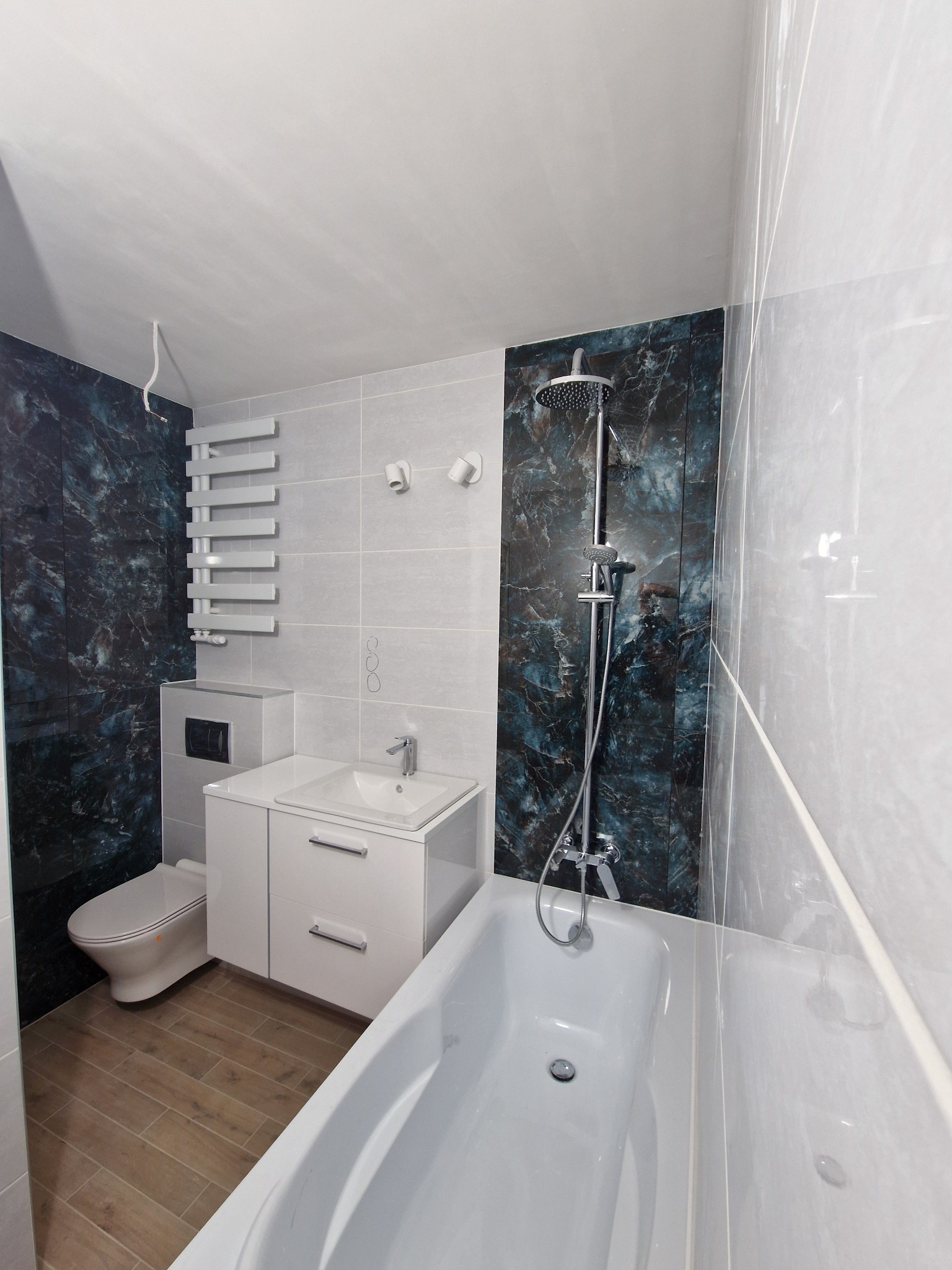 Nowoczesna łazienka po remoncie: biała armatura, marmurowe akcenty na ścianach, drewnopodobna podłoga i grzejnik drabinkowy. Minimalistyczny design.