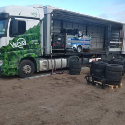 Vervo - Ciężarówka firmy Vervo z przyczepą i agregatem wewnątrz, obok sterty opon. Widoczne logo firmy i dane kontaktowe na kabinie. Transport ładunków.