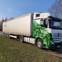 Vervo - Ciężarówka marki Mercedes-Benz z naczepą, oklejona w zielono-białe wzory geometryczne i logo firmy Vervo, zaparkowana na poboczu drogi w słoneczny dzień.