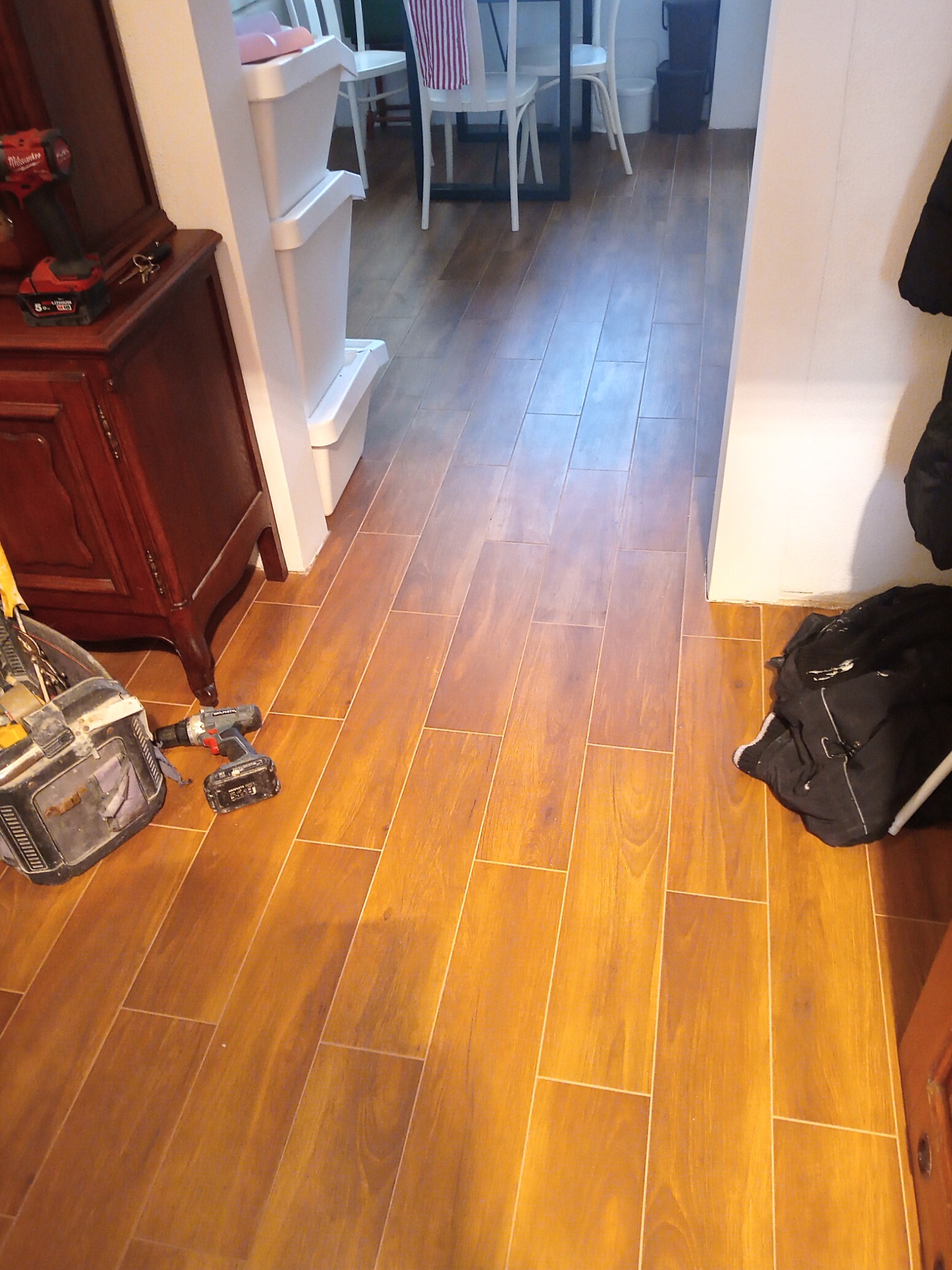 Ułożona podłoga z paneli imitujących drewno, widoczna torba narzędziowa i wkrętarka, sugerujące prace wykończeniowe w korytarzu. Ciepłe oświetlenie.