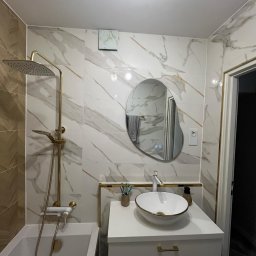 Oskar - Elegancka łazienka z marmurowymi płytkami, złotą armaturą i asymetrycznym lustrem z podświetleniem LED. Nowoczesny design z dbałością o detale.