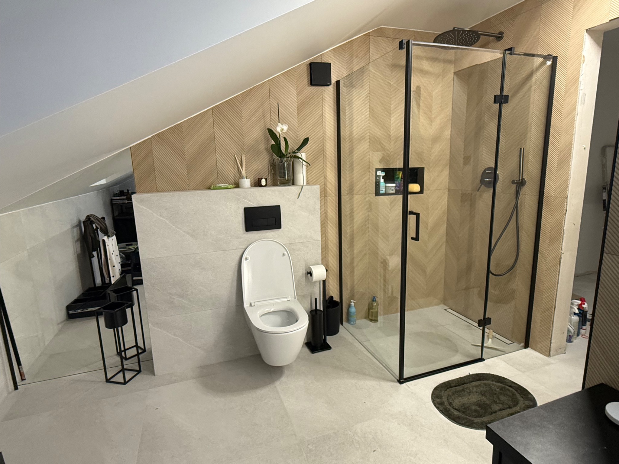 Nowoczesna łazienka na poddaszu z kabiną prysznicową typu walk-in, toaletą podwieszaną i drewnopodobnymi płytkami ułożonymi w jodełkę na ścianach.