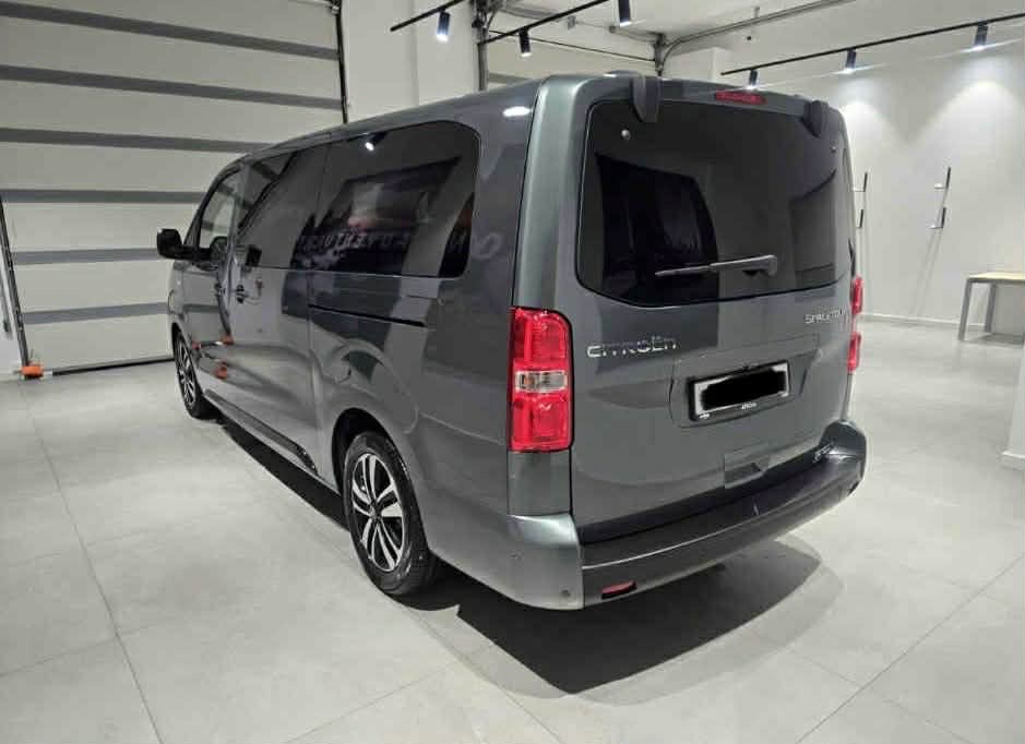 Szary bus Citroen SpaceTourer, widok z tyłu, zaparkowany w jasnym pomieszczeniu z bramą garażową. Widoczne detale: felgi, światła, logo Citroen.