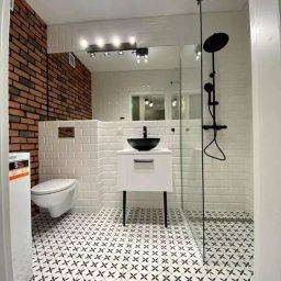 Dimfix - Nowoczesna łazienka z ceglaną ścianą, białą armaturą i czarnymi akcentami. Uwagę przykuwają wzorzyste płytki podłogowe i minimalistyczna kabina prysznicowa.
