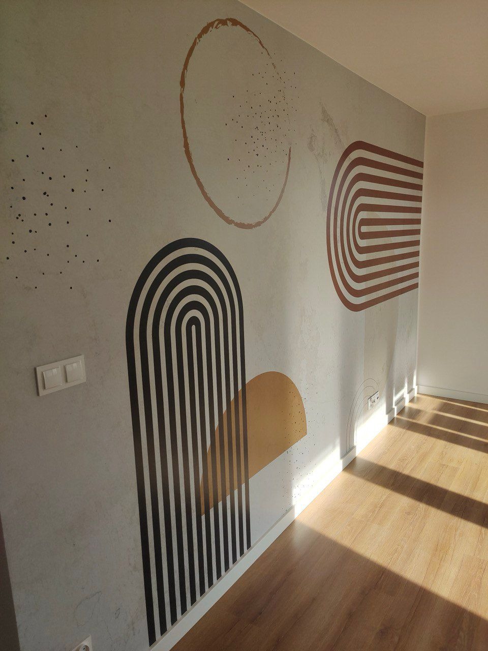 Ściana z abstrakcyjnym malunkiem w odcieniach beżu, brązu i czerni, na tle drewnianej podłogi i białej ściany. Nowoczesny design wnętrza.