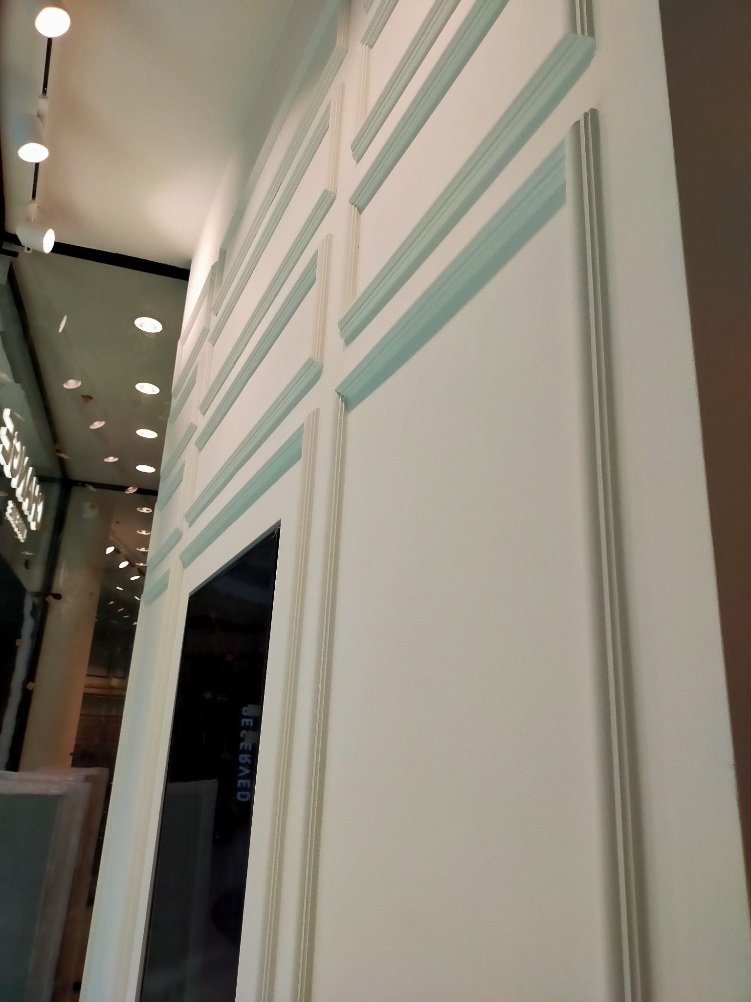 Biała ściana z dekoracyjnymi listwami i wnęką, oświetlona punktowo, widziana pod kątem. Element wykończenia wnętrza.