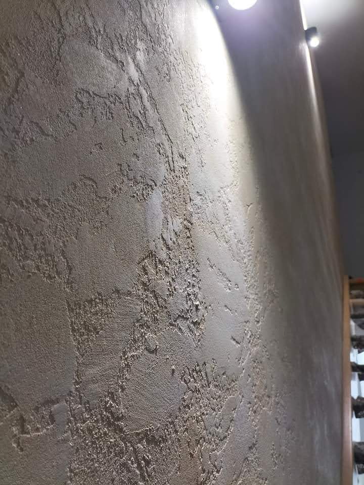 Dekoracyjna ściana z efektem strukturalnym w odcieniach beżu, oświetlona punktowo, z widoczną fakturą i nierównościami. Minimalistyczny design wnętrza.