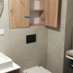 Zakład Produkcyjno - Handlowy MIKOR Andrzej Wudzki - Wykończona łazienka w Warszawie: podwieszana toaleta, szafka z drewnianymi frontami i umywalka. Minimalistyczny design, jasne płytki.