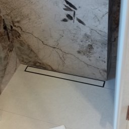 Zakład Produkcyjno - Handlowy MIKOR Andrzej Wudzki - Wykończona łazienka z marmurowymi płytkami i odpływem liniowym w podłodze. Minimalistyczny design, jasne płytki podłogowe, nowoczesne wykończenie.