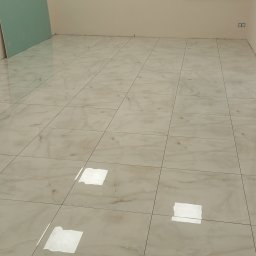 Zakład Produkcyjno - Handlowy MIKOR Andrzej Wudzki - Połyskująca podłoga z jasnych, marmurkowych płytek w nowym wnętrzu. Widoczna ściana z zieloną płytą gipsową i gniazdka elektryczne. Minimalistyczny design.