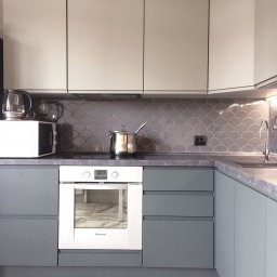 Zakład Produkcyjno - Handlowy MIKOR Andrzej Wudzki - Nowoczesna kuchnia w odcieniach szarości i beżu z płytkami w kształcie rybiej łuski. Biały piekarnik Ariston i marmurowa podłoga dodają elegancji.