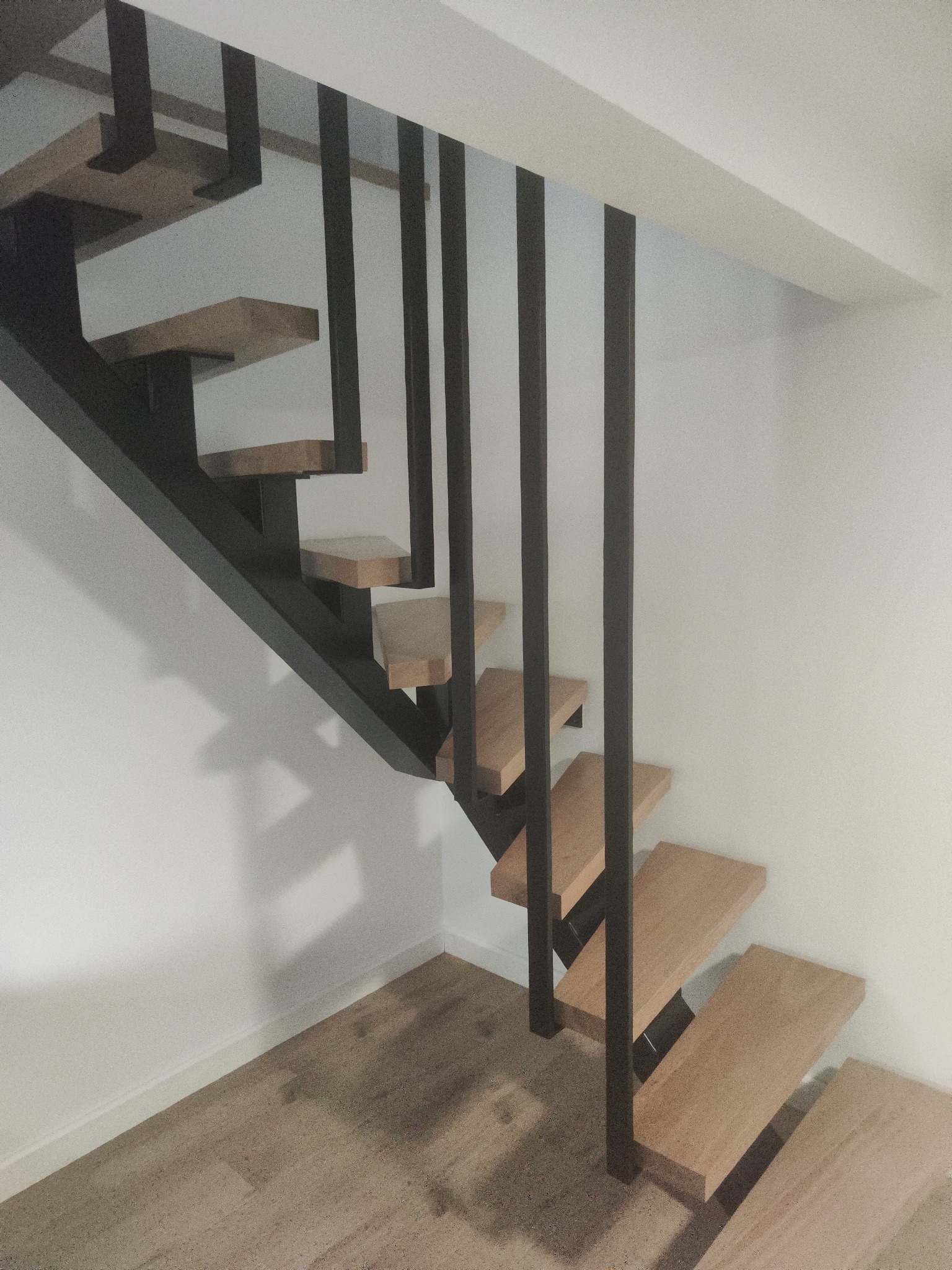 Nowoczesne schody z drewnianymi stopniami i czarną metalową konstrukcją, minimalistyczny design, jasne wnętrze, widok z dołu.