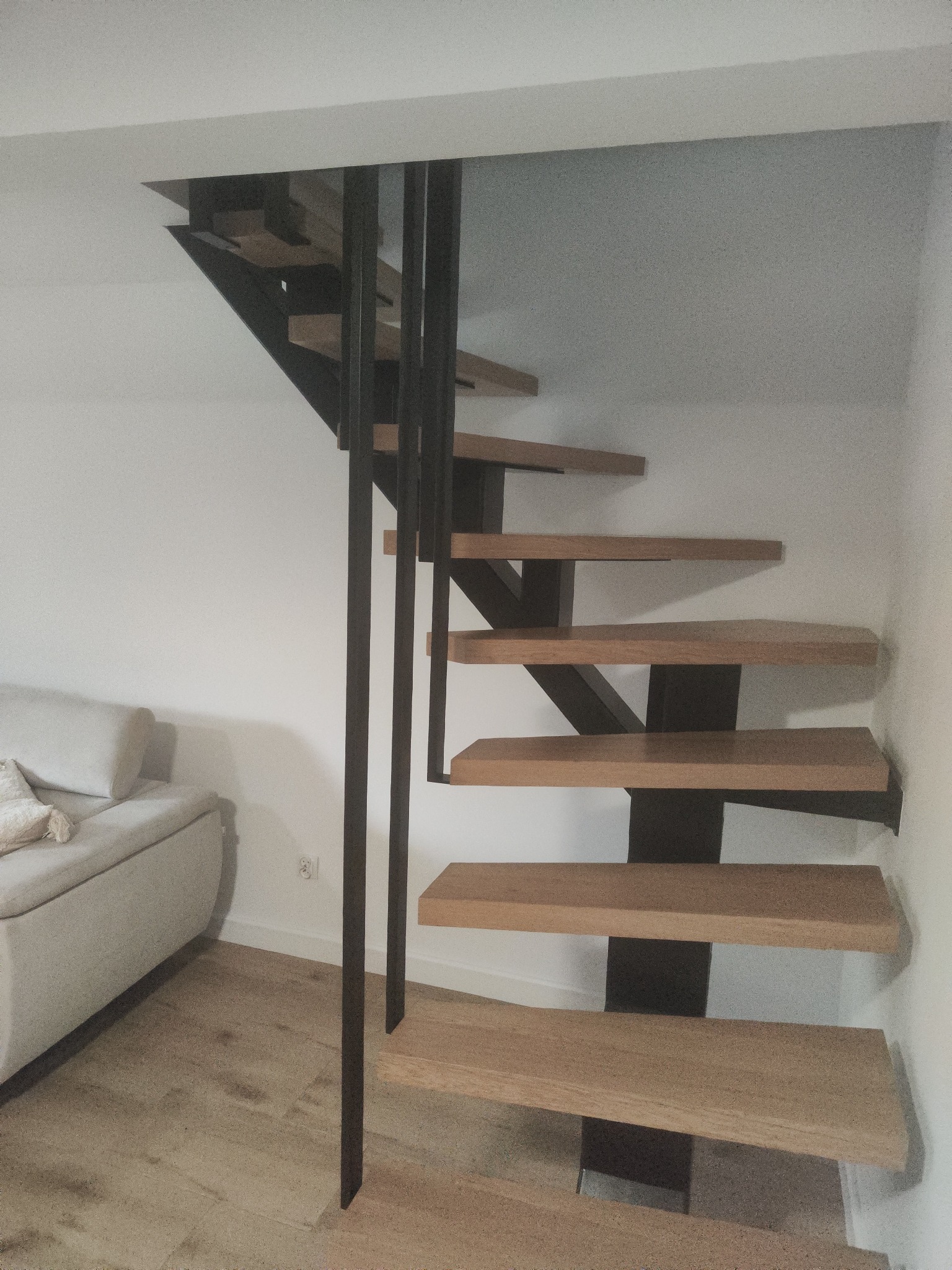 Nowoczesne schody z drewnianymi stopniami i czarną metalową konstrukcją, minimalistyczny design, jasne wnętrze, widok z dołu na górę.