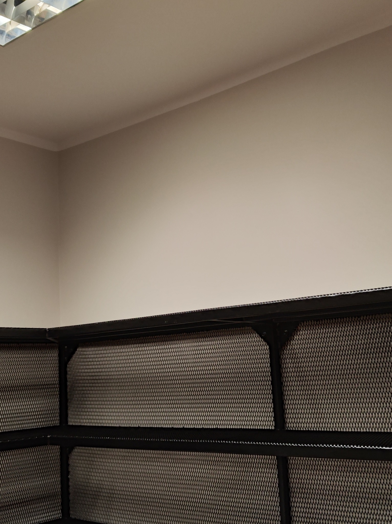 Metalowa konstrukcja z siatką w pomieszczeniu, widok z dołu, oświetlenie sufitowe. Element zabudowy lub regał z metalu.