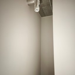 LUKA- REM Usługi remontowo- budowlane Łukasz Piekarz - Świeżo pomalowane, jednolite ściany w odcieniach szarości, z widocznym fragmentem sufitu z instalacją wentylacyjną. Minimalistyczne wnętrze po remoncie.
