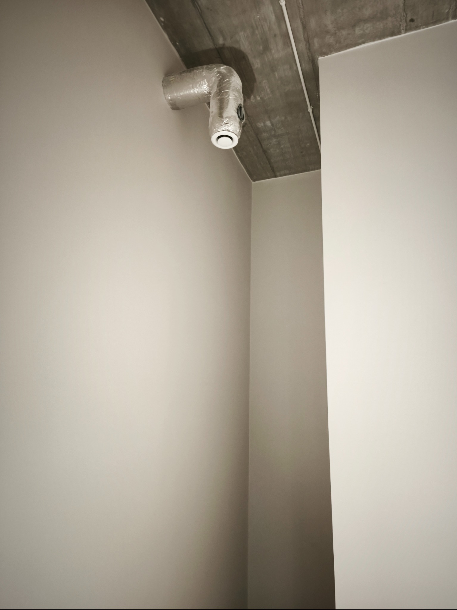 Świeżo pomalowane, jednolite ściany w odcieniach szarości, z widocznym fragmentem sufitu z instalacją wentylacyjną. Minimalistyczne wnętrze po remoncie.