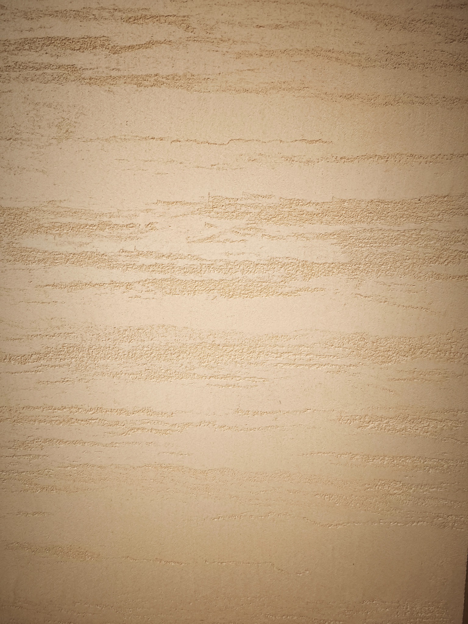 Beżowa ściana z dekoracyjną fakturą w poziome pasy, imitującą naturalny kamień. Subtelne cieniowanie podkreśla nierówności powierzchni.