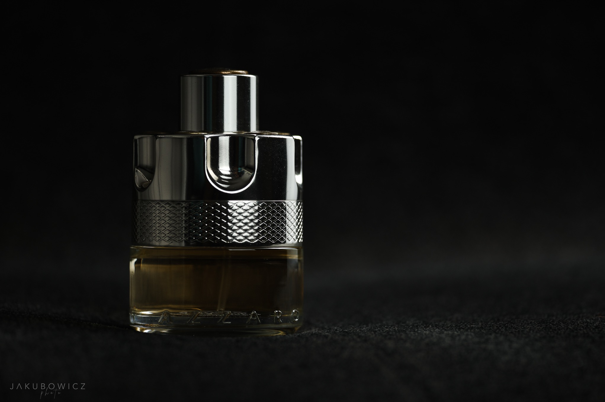 Flakon męskich perfum Azzaro Wanted w szklanej butelce z metalowym korkiem, na ciemnym tle. Minimalistyczne ujęcie z subtelnym światłem podkreśla detale.