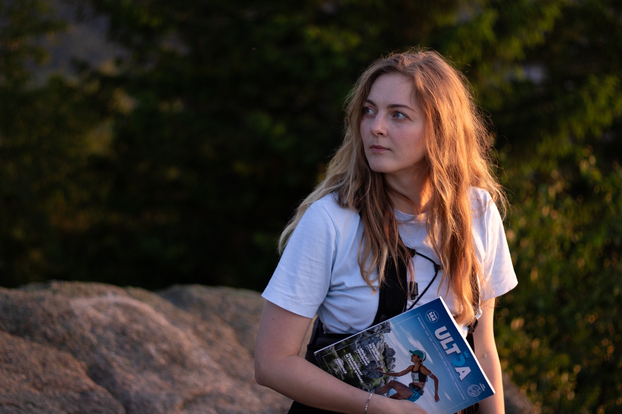 Portret kobiety z magazynem biegowym w Jeleniej Górze, na tle zieleni. Delikatne światło podkreśla naturalność i swobodę. Idealne na sesję biznesową.