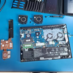 KL3DS Krystian Łukowicz - Otwarty laptop z widoczną płytą główną, wentylatorami i elementami chłodzenia, rozłożony na niebieskim podłożu, obok narzędzia i akcesoria do naprawy.