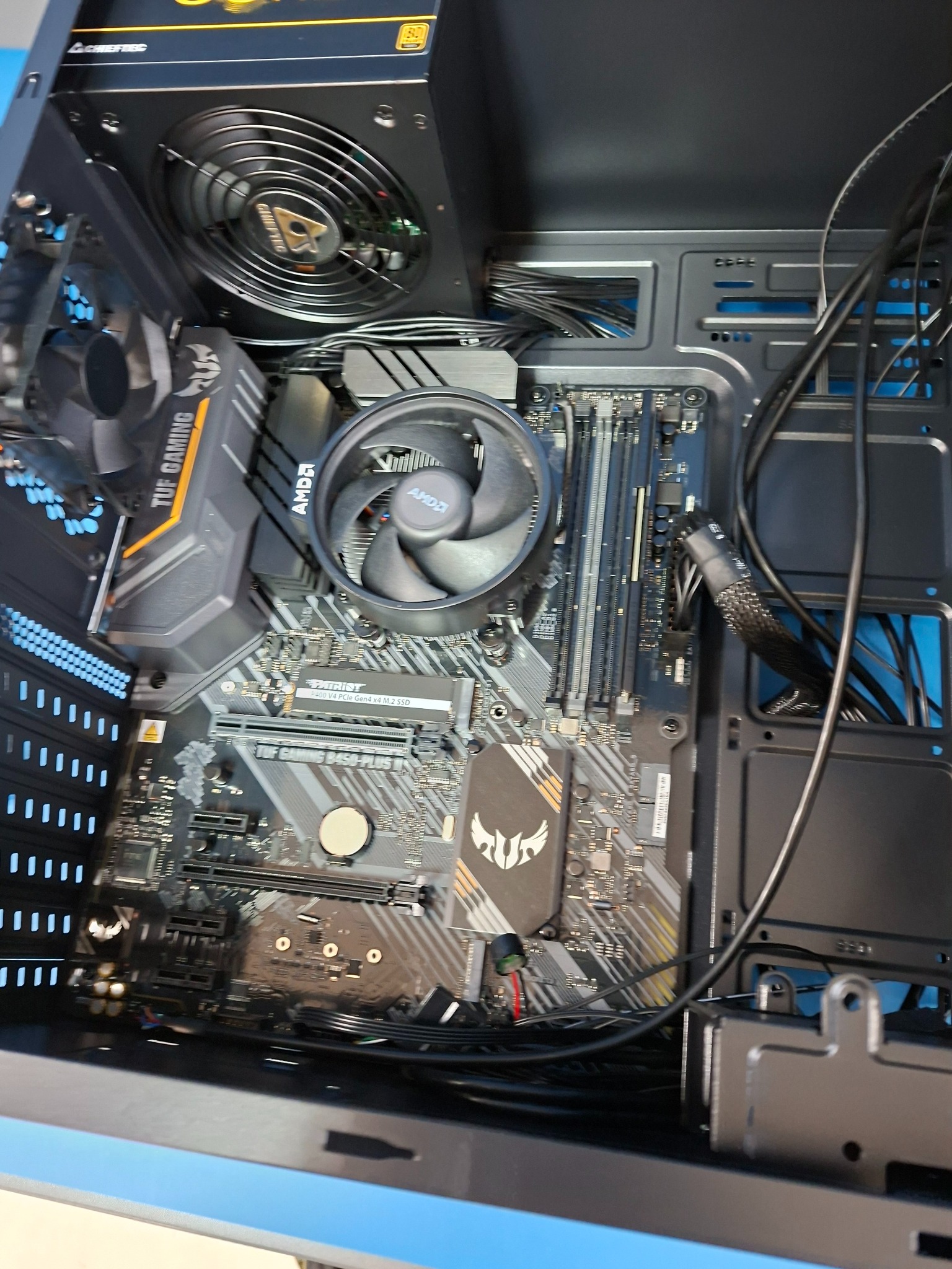 Wnętrze komputera stacjonarnego z płytą główną TUF Gaming, chłodzeniem AMD, zasilaczem Chieftec i widocznymi kablami w czarnej obudowie.