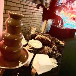 PIOTR NOWAK & CO. EVENTS - Fontanna czekoladowa i bogaty bufet słodkości z ananasem i piórami na czarnym stole, prawdopodobnie podczas eleganckiego eventu.