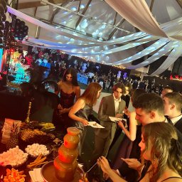 PIOTR NOWAK & CO. EVENTS - Fontanna czekoladowa na eleganckim przyjęciu z dekoracjami sufitowymi i gośćmi w strojach wieczorowych. Bufet ze słodkościami i owocami.