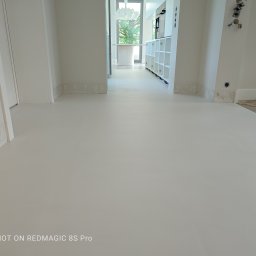 Petro Tychkovskyi - Jasna, jednolita posadzka w przestronnym wnętrzu z białymi ścianami i widocznymi instalacjami elektrycznymi. Minimalistyczny design z otwartą przestrzenią.