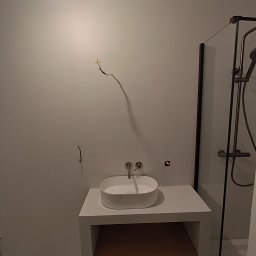 Petro Tychkovskyi - Nowoczesna łazienka w trakcie wykańczania: biała umywalka nablatowa, kabina prysznicowa z czarnymi profilami, widoczne przewody elektryczne. Minimalistyczny design.
