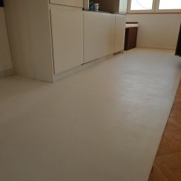 Petro Tychkovskyi - Jasna, gładka posadzka w kuchni z białymi szafkami. Widoczny fragment parkietu przy krawędzi. Minimalistyczny design, neutralne oświetlenie.