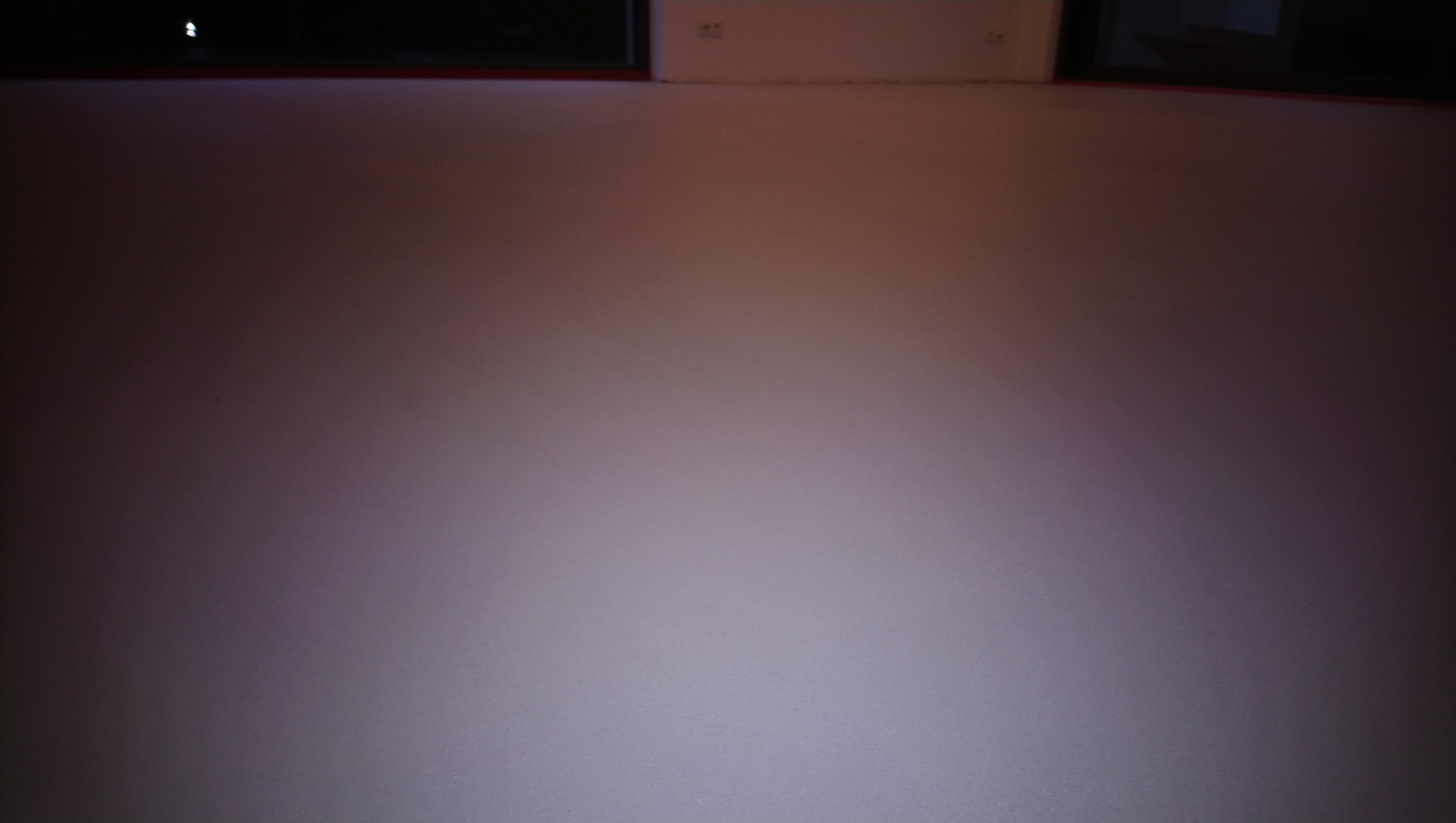 Gładka, jasna posadzka w pomieszczeniu z widocznymi gniazdkami elektrycznymi przy ścianie. Minimalistyczne wykończenie podłogi w neutralnej kolorystyce.