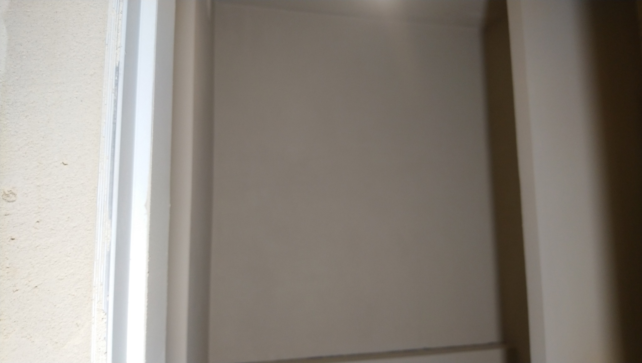 Ściana w odcieniach beżu z widoczną białą ramą drzwiową. Widoczne niedoskonałości na ścianie i ramie, sugerujące etap prac wykończeniowych.