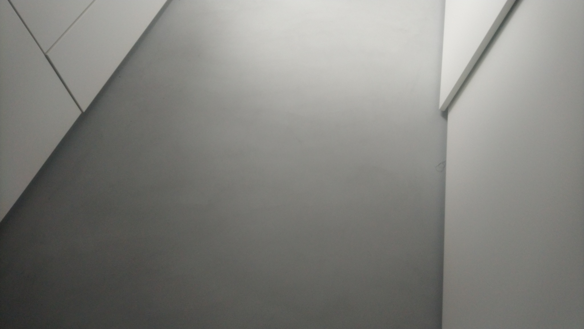 Szara ściana z wykończeniem w postaci białych paneli, tworzących geometryczny wzór. Minimalistyczny design wnętrza, świeżo po remoncie.