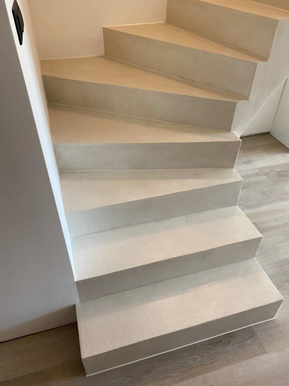 Schody wewnętrzne wykończone jednolitą, beżową powłoką, prawdopodobnie mikrocementem. Widoczne detale wykończenia i subtelna faktura materiału.