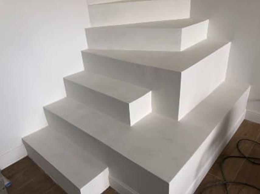 Białe, minimalistyczne schody z mikrocementu, widok z dołu, z delikatnym oświetleniem podkreślającym gładką powierzchnię. Widoczne drewniane panele podłogowe.