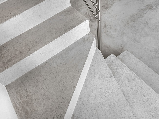 Betonowe schody z metalową poręczą, widok z góry, minimalistyczny design, szara kolorystyka, surowy styl wykończenia wnętrza, nowoczesne budownictwo.