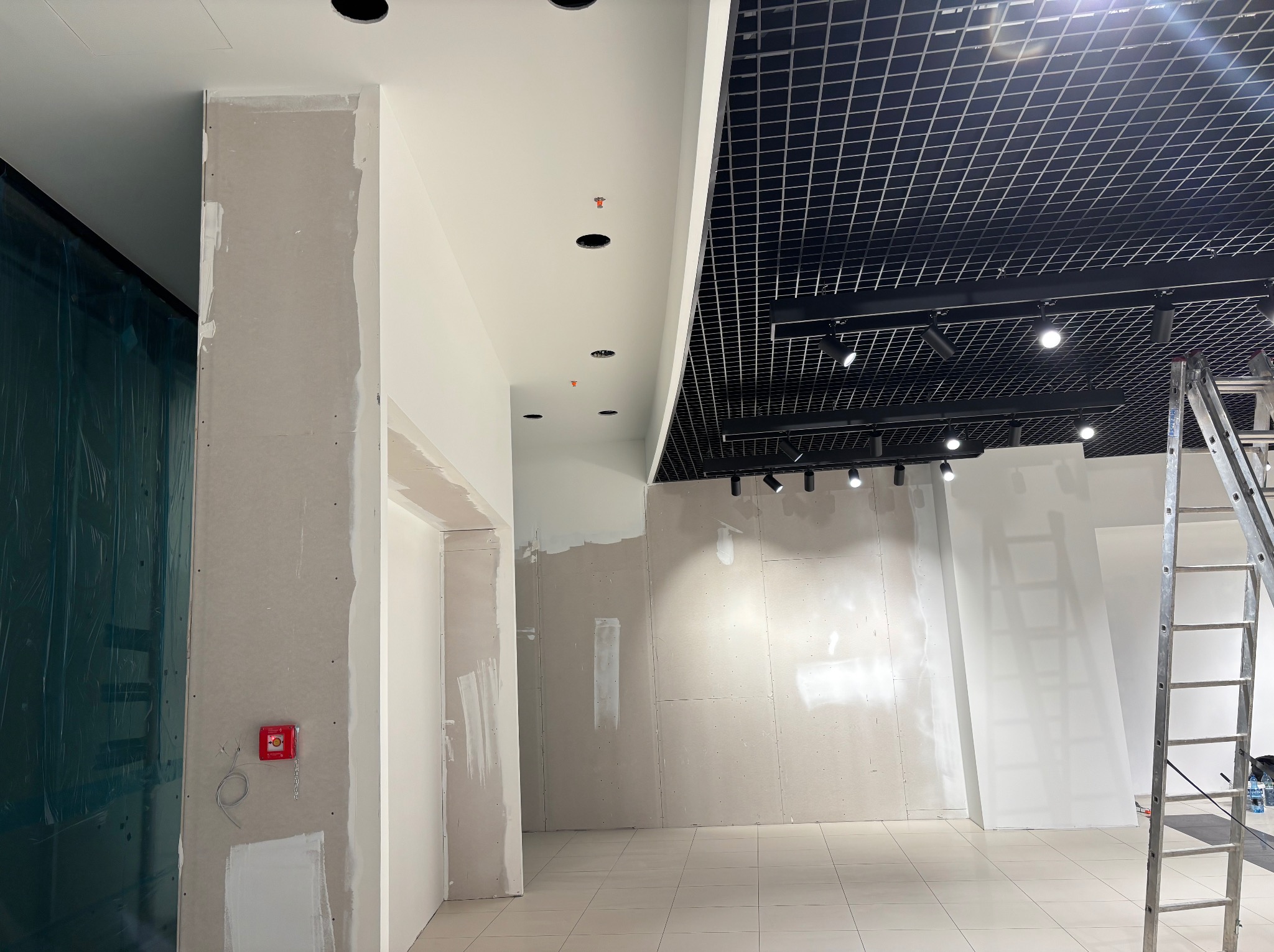 Wnętrze biura w trakcie prac wykończeniowych: ściany z płyt karton-gips, częściowo wyszpachlowane, sufit z kratką i oświetleniem, drabina aluminiowa z boku.