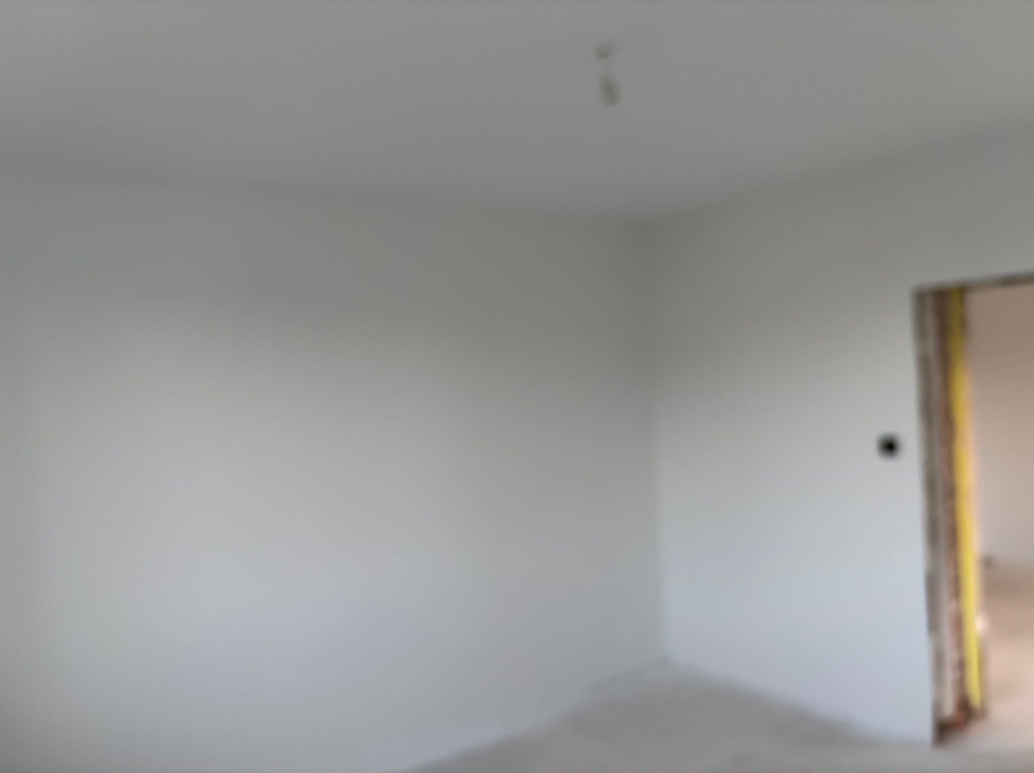 Wnętrze pokoju po malowaniu na biało, widoczne świeżo pomalowane ściany i futryna drzwi. Minimalistyczny wystrój, surowe wykończenie.