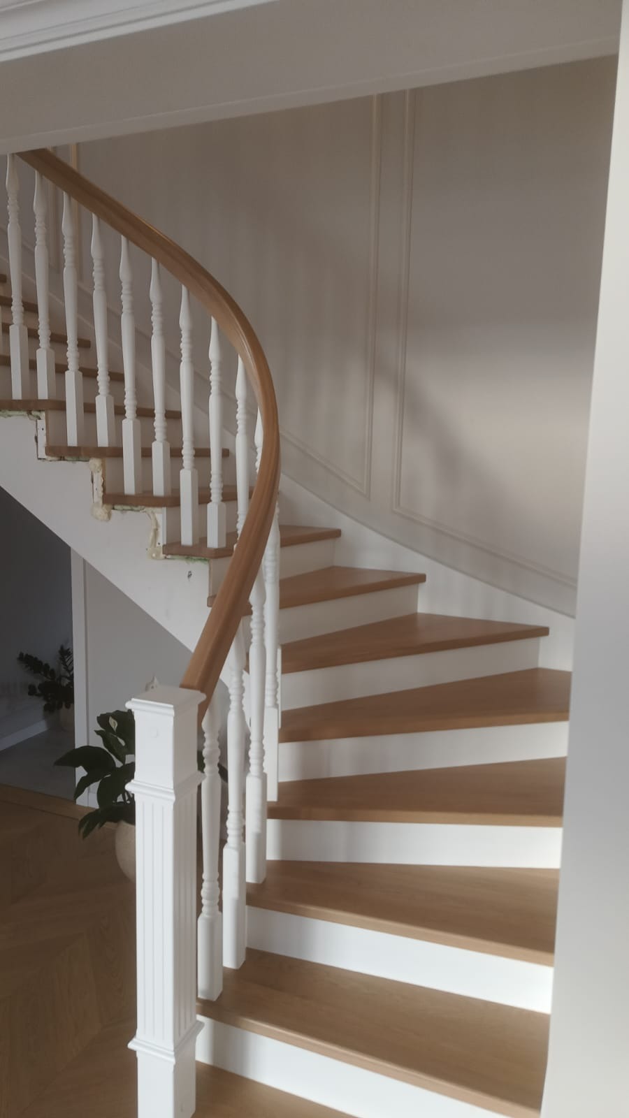 Zakręcone schody drewniane z białymi balustradami i drewnianymi stopniami, widok z dołu, eleganckie wykończenie wnętrza, jasne kolory, dekoracyjne panele ścienne.