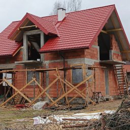 AD-BUD usługi remontowo budowlane - Ceglany dom w trakcie budowy z czerwonym dachem, widoczne rusztowania i niezabezpieczone okna. Surowy stan, brak wykończenia elewacji.