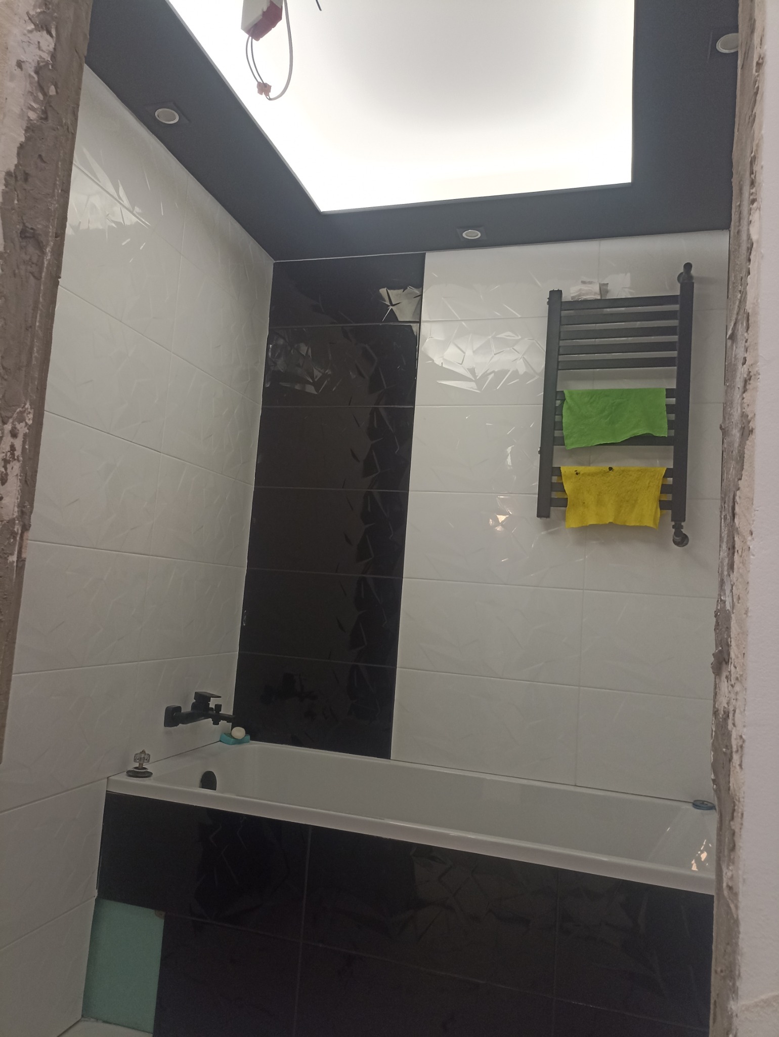 Wykończona łazienka z czarno-białymi płytkami o wzorzystej strukturze, grzejnikiem drabinkowym z ręcznikami i podwieszanym sufitem z oświetleniem punktowym.