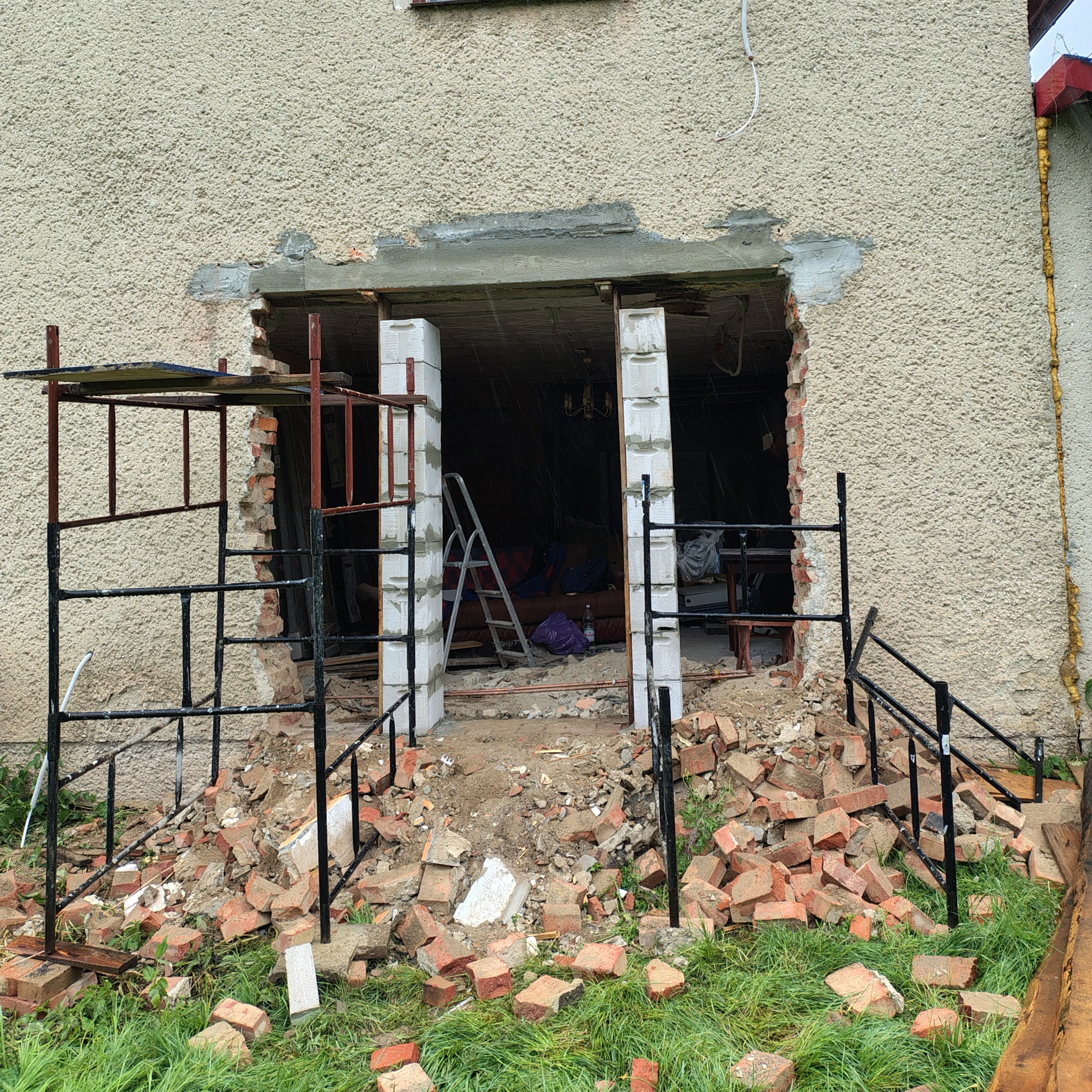 Otwór w elewacji budynku w Śremie, z widocznymi rusztowaniami i gruzem, przygotowany pod montaż drzwi lub okna. Prace remontowe w toku.